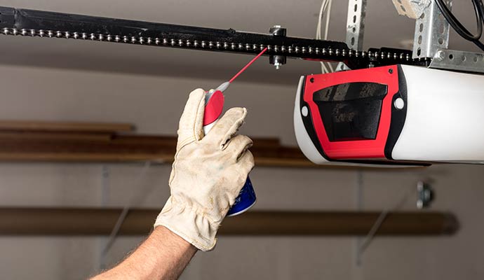 Applying professional lubricant spray to garage door opener track during a tune-up