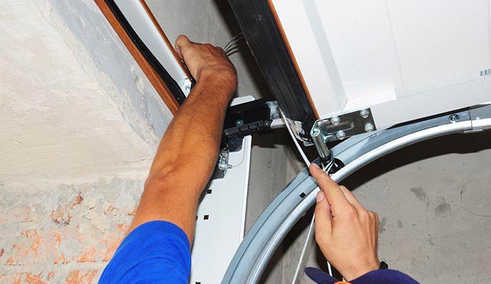Technician inspecting garage door cables and rollers during a safety inspection in Albany